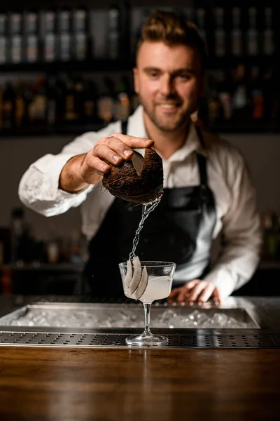 Улыбающийся бармен держит кусок кокоса и наливает кокосовое молоко в стекло — стоковое фото