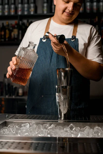 Cantinero masculino vertiendo bebida alcohólica de jigger de acero en la taza del agitador — Foto de Stock
