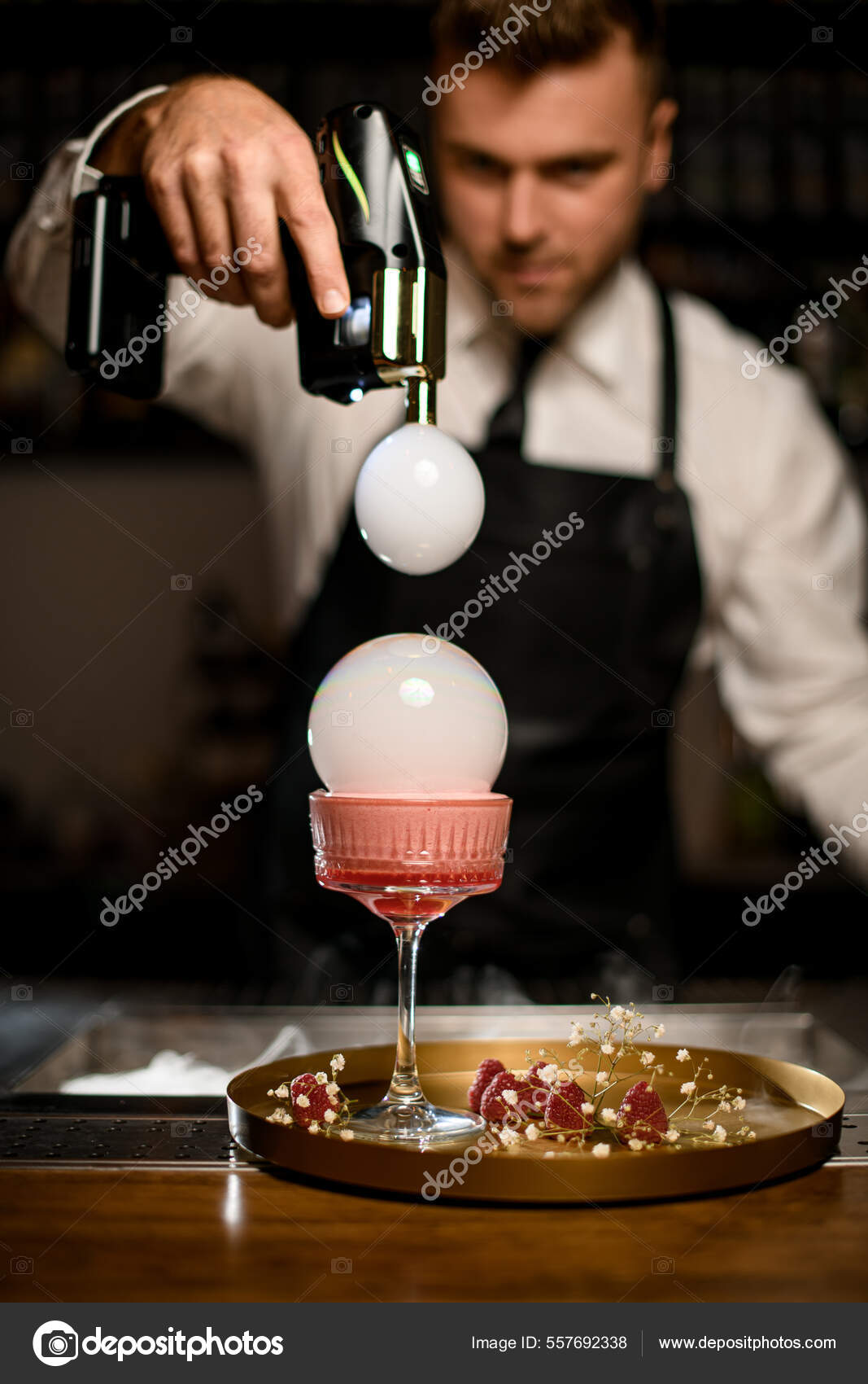Hand of bartender holds flavour blaster and decorate glass with