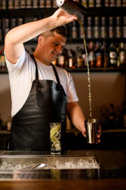 Erkek barmen ustalıkla bir bardaktan diğerine kokteyl doldurur.