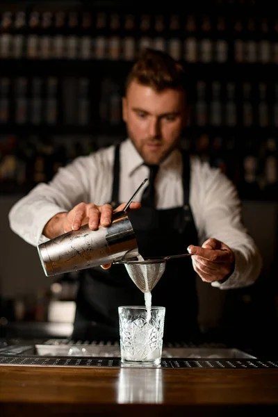Barman trzyma shaker i wlewa biały płyn do szkła przez sito — Zdjęcie stockowe
