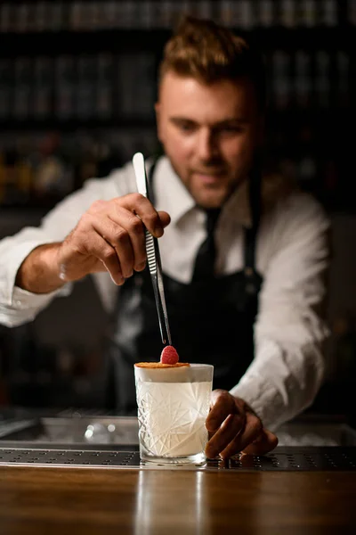 Мужская рука с пинцетом и аккуратно налейте малину на стакан с коктейлем — стоковое фото