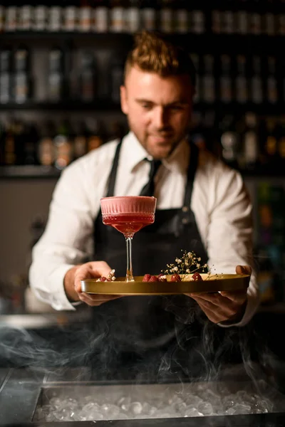 Mano de barman sostiene bandeja redonda con frambuesas y flores y copa de cóctel en ella —  Fotos de Stock