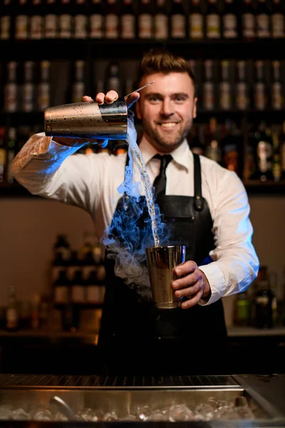 Homme souriant barman verse habilement un cocktail fumant d'une tasse shaker à l'autre — Photo