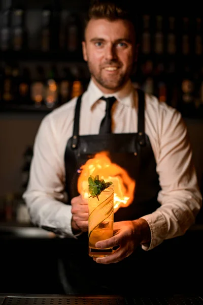 Barmen elinde salatalık dilimleri ve nane şekeri ile bir bardak kokteyl tutuyor ve onu ateşe veriyor. — Stok fotoğraf