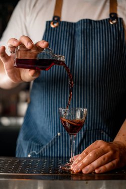 Barmen adam küçük bir şişe tutuyor ve alkollü bir içeceği bardağa dolduruyor.