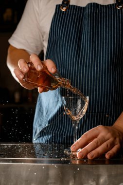 Adam küçük bir şişe tutuyor ve alkollü bir içkiyi bardağa dolduruyor.