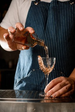Barmen elinde bir bardak tutuyor ve bardağın yarısını alkollü içecekle dolduruyor.