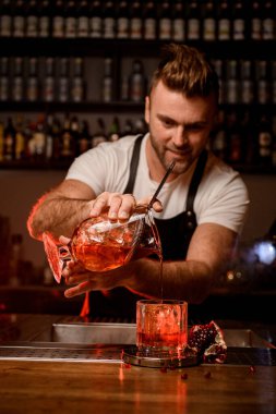 Barmen nazikçe süzgeçle karıştırma bardağını tutuyor ve viski bardağına sıvı döküyor.