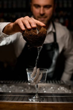 Barmen dikkatle hindistan cevizinden bardağa su dolduruyor.