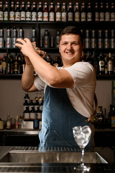 Cantinero profesionalmente sostiene por dos manos coctelera vidriosa con cóctel alcohólico frío y lo sacude. — Foto de Stock