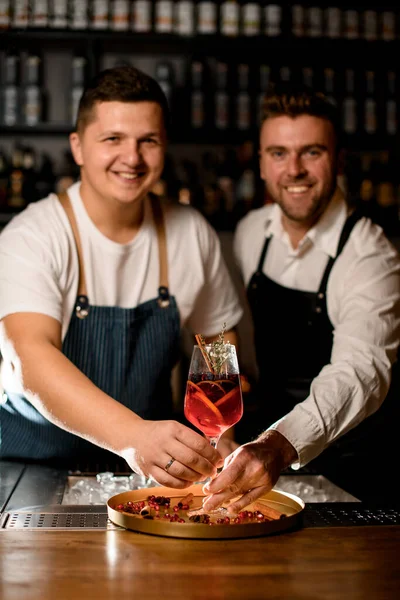 İki genç barmen, portakallı, üzümlü, çiçekli ve tarçınlı bir kokteyl sunar. — Stok fotoğraf