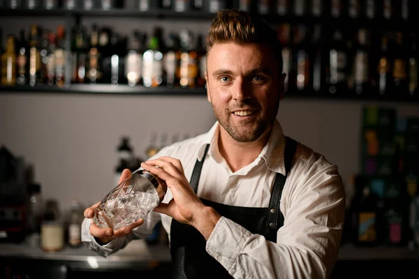 Ung stilig leende bartender i bar interiör håller glasartad shaker — Stockfoto