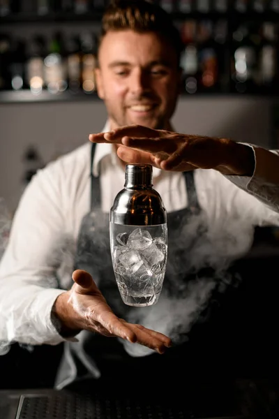 Joven barman guapo en el interior de la barra hábilmente lanza un agitador con hielo en el aire —  Fotos de Stock