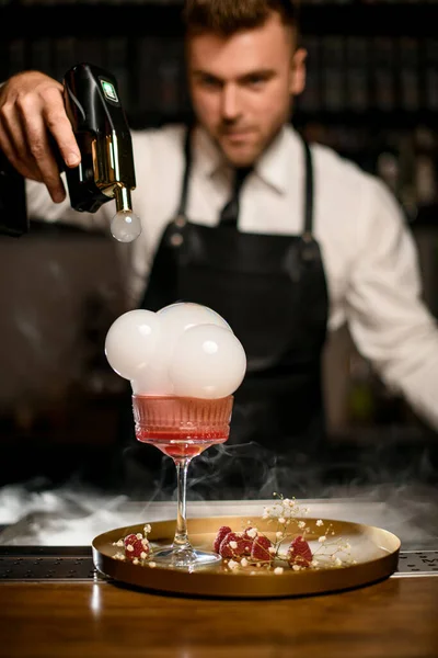 Cantinero decora cóctel espumoso rosa en copa de champán haciendo burbuja de aire de humo — Foto de Stock
