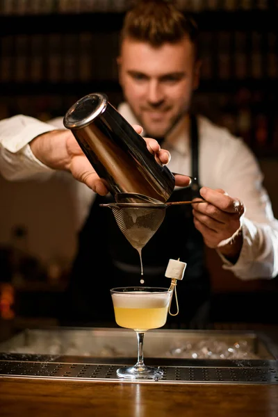 Uomo barista filtra con attenzione cocktail alcolici da tazza shaker in acciaio in vetro attraverso setaccio — Foto Stock