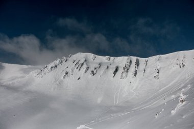 Büyük dağ yamaçları beyaz kar ve parlak mavi gökyüzü ile kaplıdır.