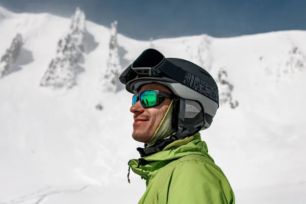 Güneş gözlüklü bir adam ve kar kaplı dağların arka planında bir kayak kaskı. — Stok fotoğraf
