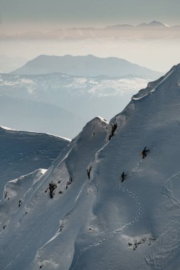 Karla kaplı dağ yamacının muhteşem manzarası boyunca kayakçı grupları tırmanıyor.