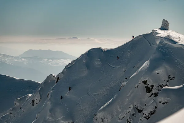 Uitzicht op de bergtop bedekt met sneeuw langs de piste waarvan groepen skiërs klimmen — Stockfoto