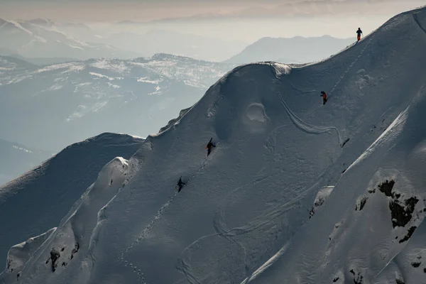 Grande vista da encosta da montanha coberta de neve ao longo do qual os grupos de esquiadores escalam — Fotografia de Stock