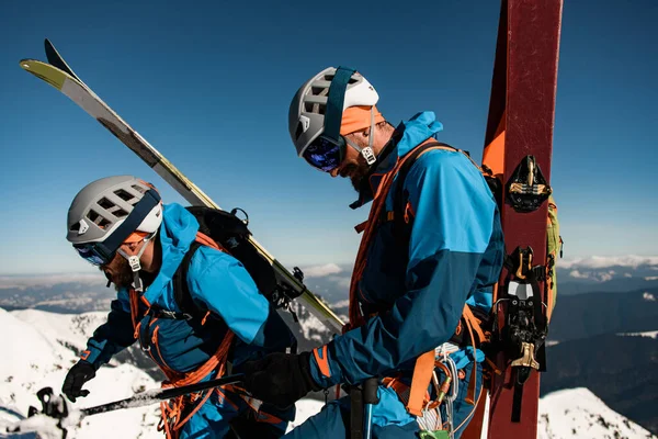 Close-up of men skiers with ski equipment against backdrop clear blue sky. — Fotografia de Stock
