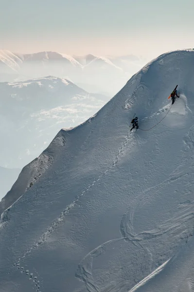 Вид з повітря на гірський схил, покритий снігом, уздовж якого піднімаються групи лижників — стокове фото