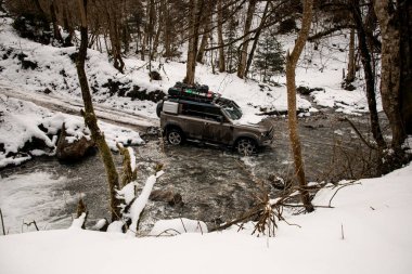 Kışın bir dağ nehrinden geçen off-road aracının yüksek açılı görüntüsü