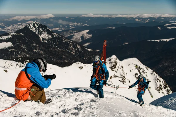 Fotografo scatta foto di sciatori maschi con attrezzatura da sci arrampicata su un pendio innevato — Foto Stock