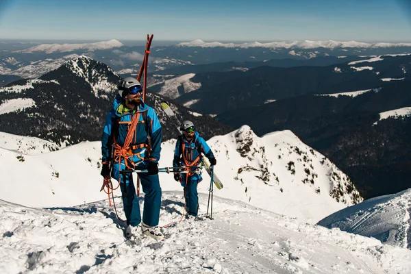 Skiers in bright ski suits with ski equipment on snowy ridge. — стоковое фото