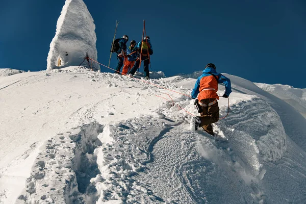 Вид снизу на человека в лыжном костюме, держащего верёвку и карабкающегося по снежному склону горы — стоковое фото