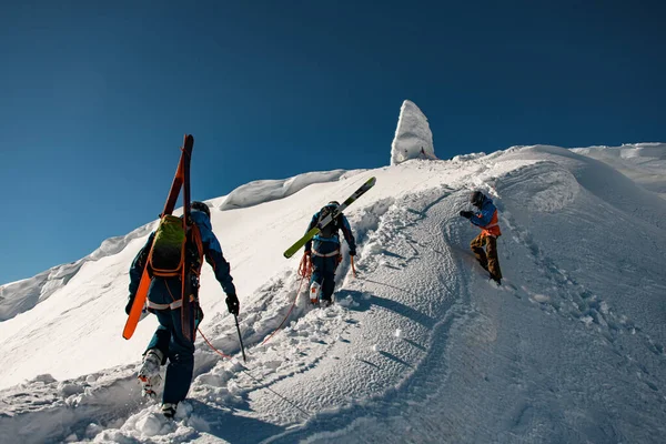 Группа лыжников с рюкзаками и лыжным снаряжением поднимается по снежному хребту — стоковое фото
