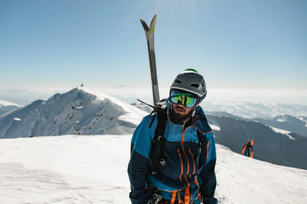 Portrait of man in bright ski suit with skis on his back against the background of winter landscape — стоковое фото