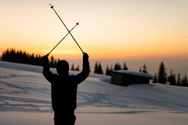 Rear view of man with ski poles crossed over his head against the backdrop of sunset sky — ストック写真