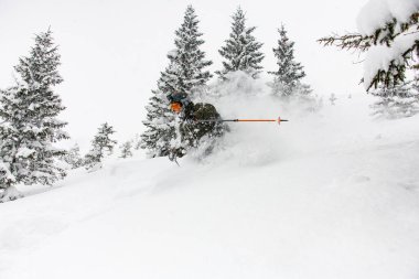 Kayakçı karla kaplı bir dağ yamacından iniyor ve etrafını karla kaplıyor.