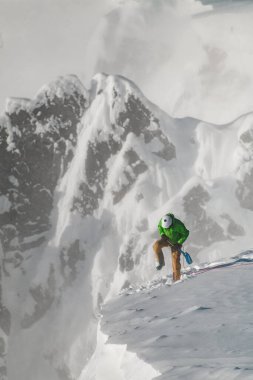 Büyük karla kaplı dağ uçurumu ve tepesinde ekipman olan bir tırmanışçı.