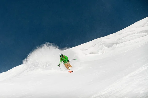 Skidåkare nedför en snötäckt bergssluttning och snöstänk bakom sig — Stockfoto