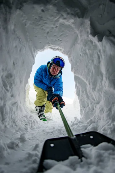 Вид из снежной пещеры человека, убирающего снег лопатой — стоковое фото