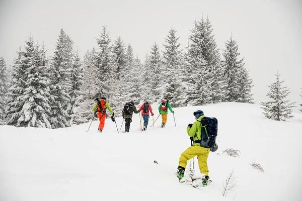 Лыжник в зеленом и желтом лыжном костюме с рюкзаком фотографирует группу лыжников — стоковое фото