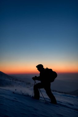 Gökyüzü ve güneşin doğuşuna karşı karla kaplı bir tepede kayakçı