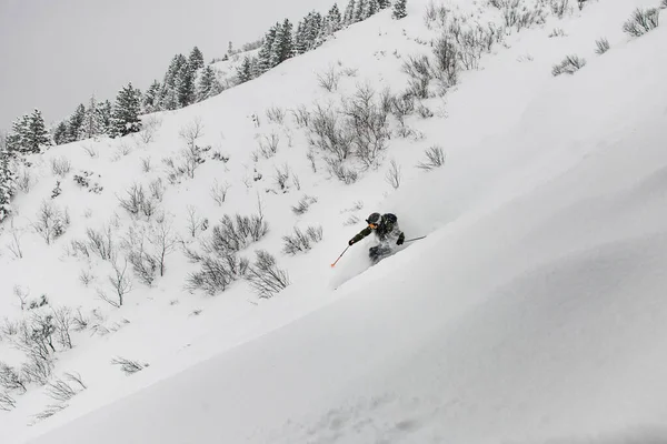 Фрирайдер в шлеме, лыжном костюме и очках катается на лыжах по заснеженным склонам — стоковое фото