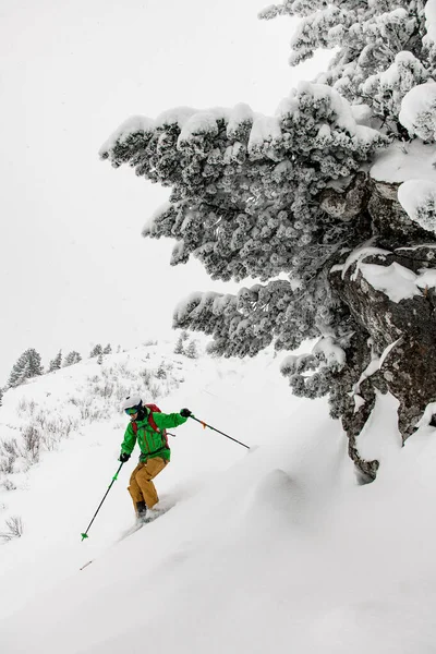 Narciarz w jasnym stroju narciarskim, hełmie i goglach zjeżdżający po pokrytych śniegiem stokach — Zdjęcie stockowe