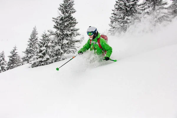 Esquiador masculino em terno de esqui verde, capacete e óculos deslizando para baixo encostas cobertas de neve em esquis — Fotografia de Stock