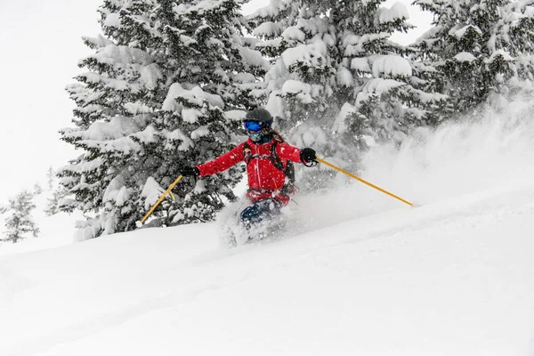 Narciarka w jasnym stroju narciarskim, kasku i goglach zjeżdżająca po pokrytych śniegiem stokach na nartach — Zdjęcie stockowe