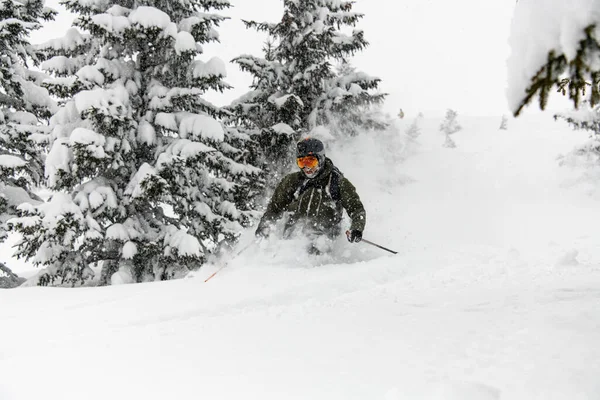 Esquiador masculino em terno de esqui, capacete e óculos deslizando rapidamente pela encosta da montanha nevada — Fotografia de Stock