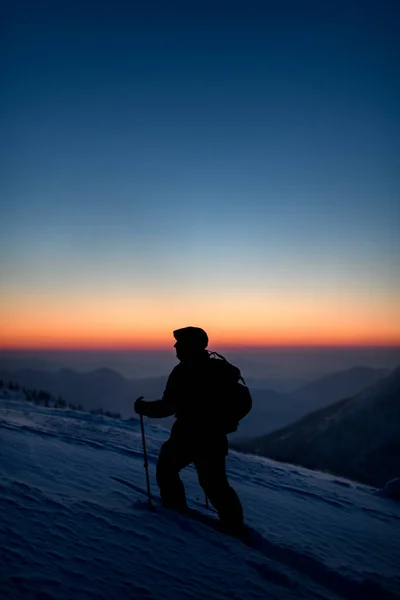 Man in ski suit with ski poles on deep powdery snow against the backdrop of sunset sky and mountain peaks — стоковое фото