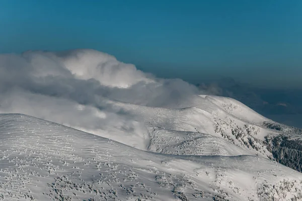 Snöiga bergstoppar höljda i moln med blå himmel på bakgrunden — Stockfoto