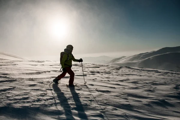 Homem em terno de esqui verde e vermelho com postes de trekking caminha através de neve pulverulenta profunda — Fotografia de Stock