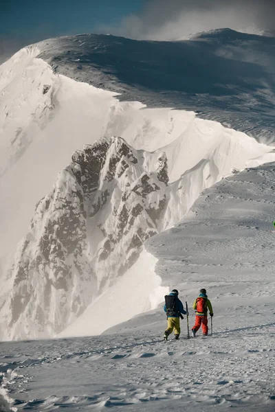 两名携带滑雪器材的男子在冬季雪山边的小径上行走. — 图库照片