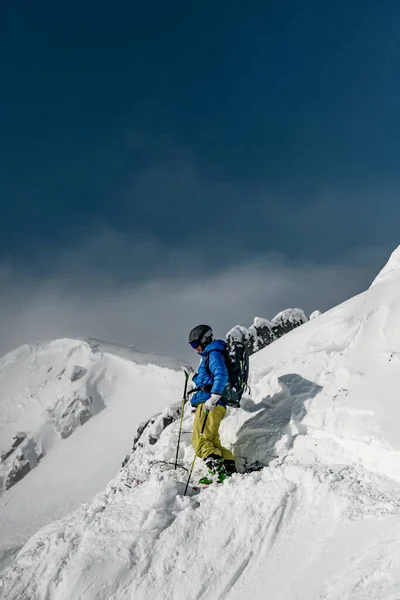 Skier man in goggles, helmet and blue and yellow ski suit doing ski touring in winter mountai — ストック写真